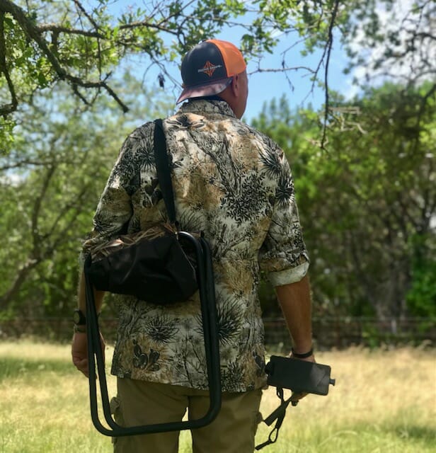 A man dressed in camoflauge holding a camera in the middle of a field